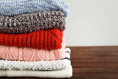 Folded knitted sweaters on grey background clipart