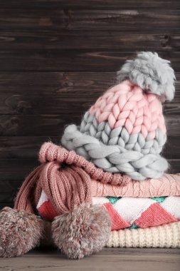 Ahşap arka planda şapka ve eşarplı katlanmış süveterler.