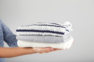 Gri arka planda katlanmış örgü süveter tutan kadın elleri