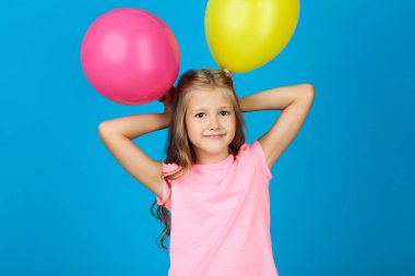 Mavi arka planda kauçuk balonları olan güzel küçük kız.