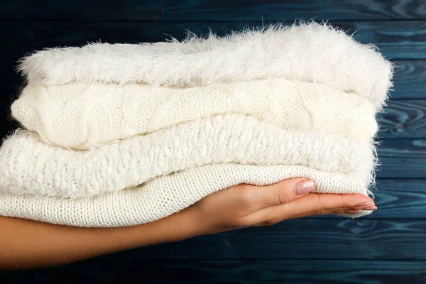 Mani femminili che tengono maglioni lavorati a maglia piegati su dorso di legno blu — Foto Stock