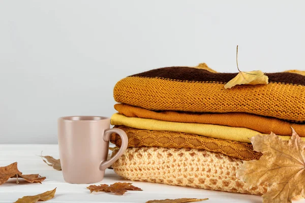 Folded sweaters with autumn leafs and cup of tea on grey backgro