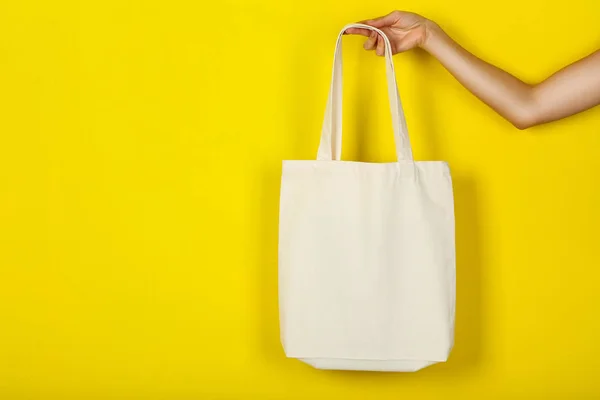 Main féminine tenant un sac écologique en coton blanc sur fond jaune — Photo