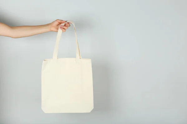 Main féminine tenant un sac écologique en coton blanc sur fond gris — Photo