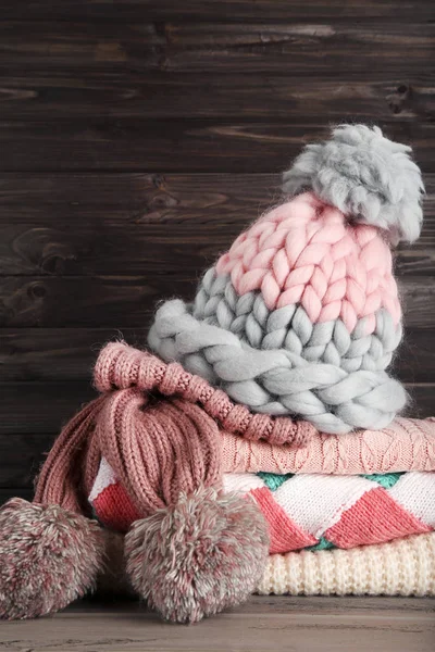 Ahşap arka planda şapka ve eşarplı katlanmış süveterler.