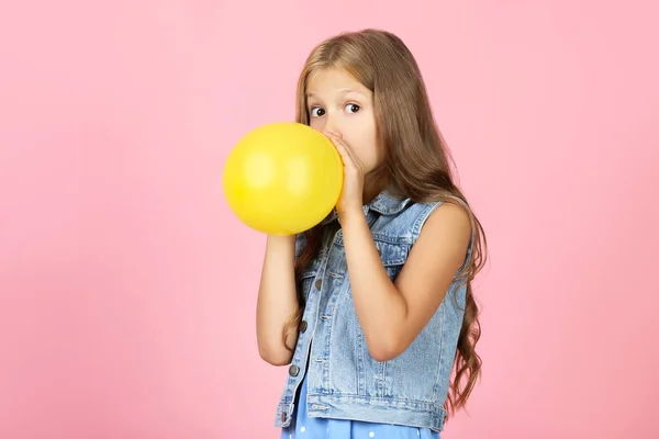 Söt liten flicka blåser gul ballong på rosa bakgrund — Stockfoto