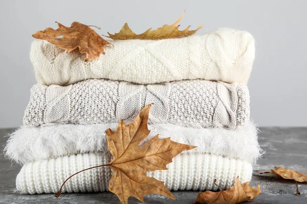 Folded sweaters with autumn leafs on grey background — Stock Photo, Image