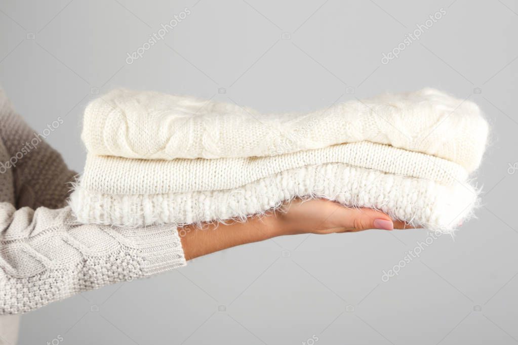 Female hands holding folded knitted sweaters on grey background