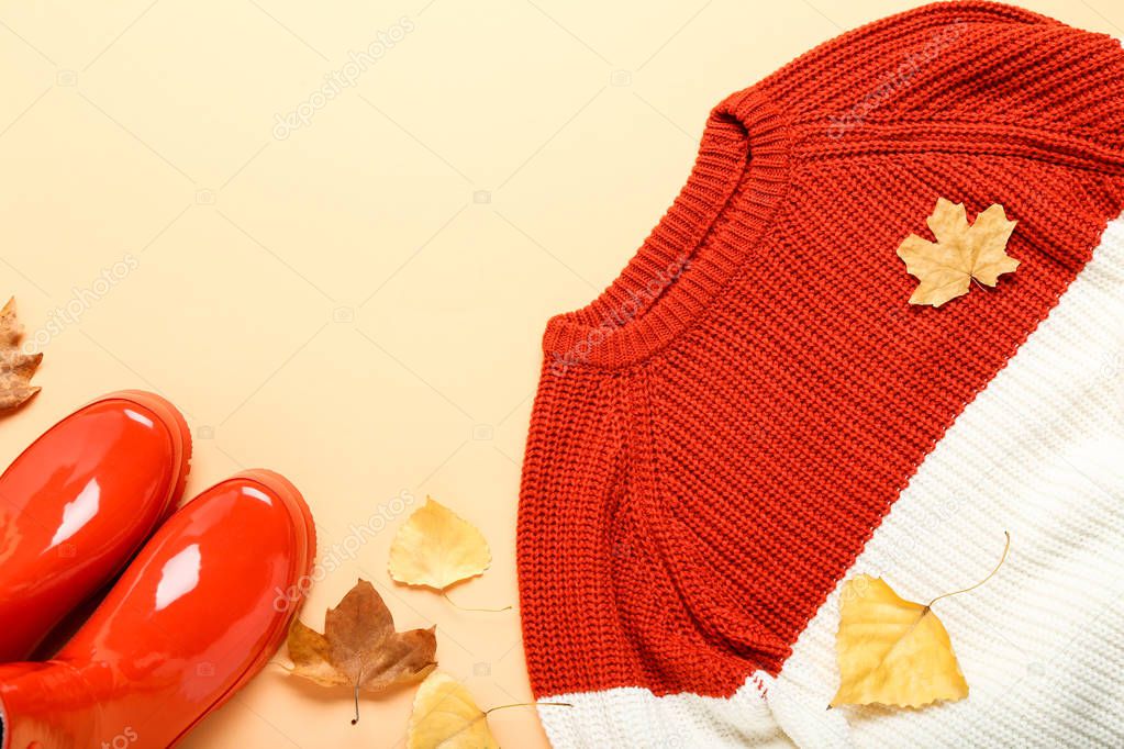 Woolen sweater with autumn leafs and red rubber boots on beige b