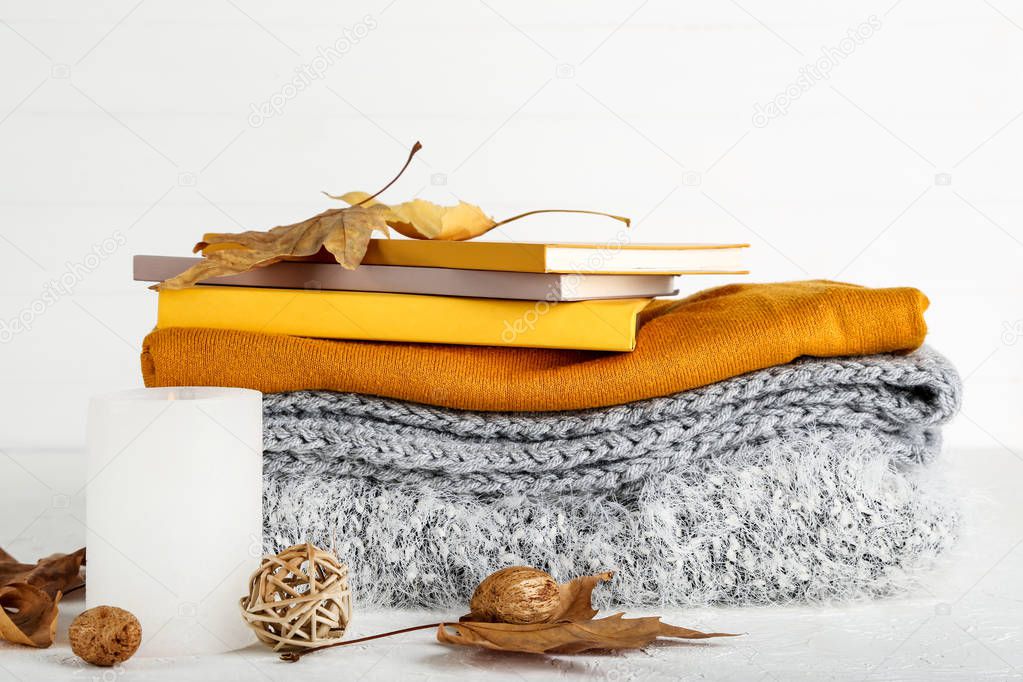 Folded sweaters with autumn leafs, candle and notepads on white 