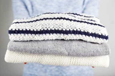 Gri arka planda katlanmış örgü süveter tutan kadın elleri