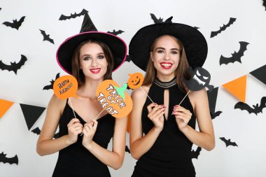 Siyah kostümlü iki genç kadın ellerinde kağıt balkabaklarıyla