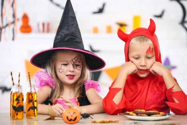Молодая девушка и мальчик в костюмах на Хэллоуин сидят за столом — стоковое фото