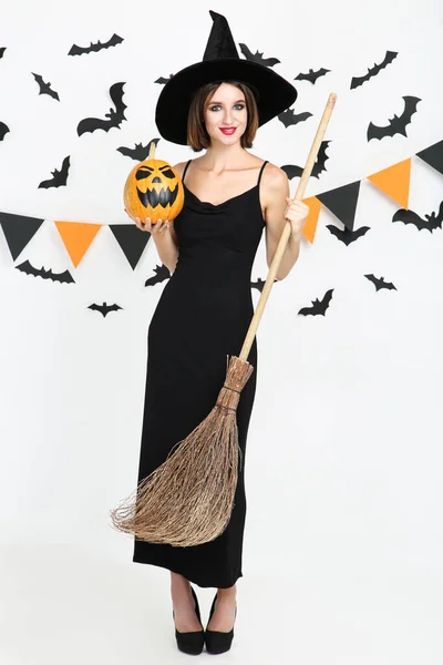 Joyeux jeune femme en costume d'Halloween tenant balai et citrouille — Photo