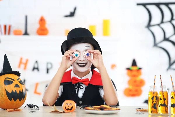 若いです男の子でハロウィンの衣装でテーブルのそばに座って保持 — ストック写真