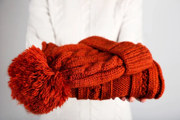 Γυναικεία χέρια που κρατούν διπλωμένο πλεκτό πουλόβερ και καπέλο σε γκρι πλάτη — Φωτογραφία Αρχείου