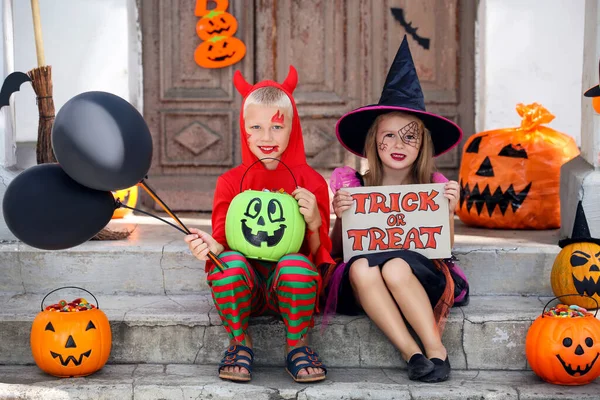 Giovane ragazza e ragazzo in costumi di Halloween seduto sul portico con p — Foto Stock