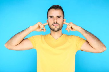 Mavi arka planda kulakları parmaklarıyla kapatan genç bir adamın portresi