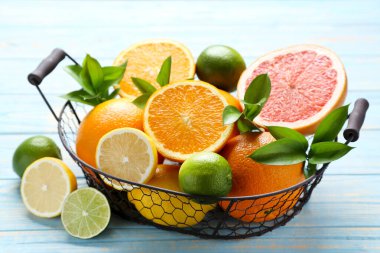 Ahşap masada sepette yeşil yapraklarla narenciye meyveleri