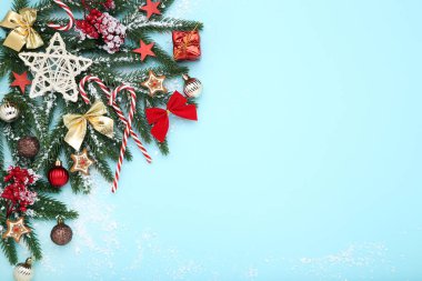 Mavi arka planda oyuncakları ve şekerlemeleri olan Noel ağacı dalları