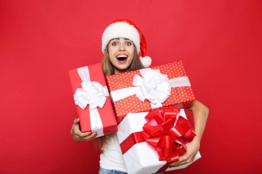 Güzel bir kadın Noel Baba şapkası takıyor ve kırmızı üzerinde hediye kutuları taşıyor. 