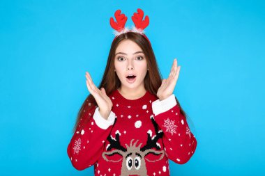 Noel süveteri ve mavi arka planda kırmızı boynuzları olan güzel bir kadın.