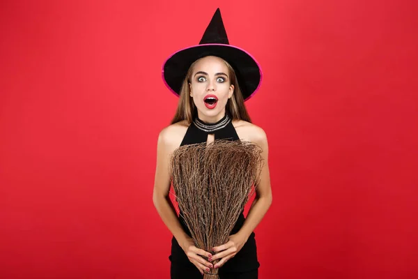 Piękna kobieta w Halloween kostium gospodarstwa miotł na czerwonym ekspresyjne — Zdjęcie stockowe