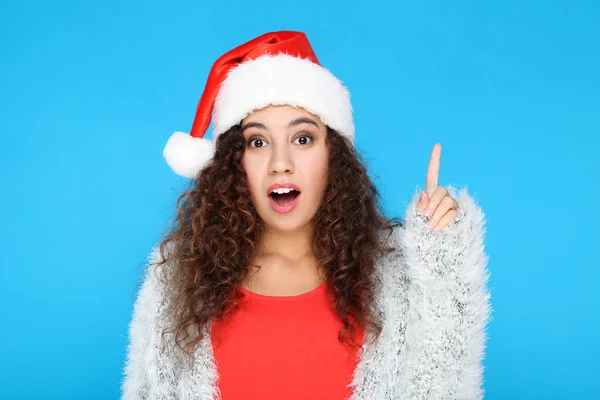 Noel Baba şapkalı güzel Amerikalı kadın mavi arka planda parmağını gösteriyor. — Stok fotoğraf