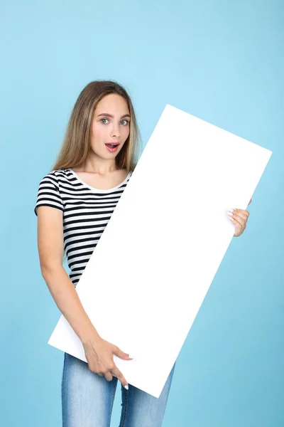 Beautiful young woman holding white blank board on blue backgrou — Stock Photo, Image