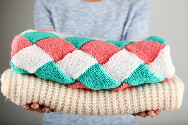 Female hands holding folded knitted sweaters on grey background — Stock Photo, Image