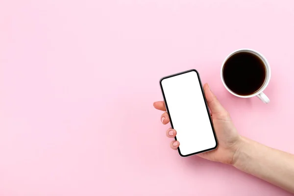 Смартфон в руке с чашкой кофе на розовом фоне — стоковое фото