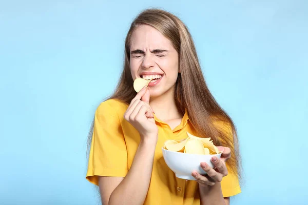 Young beautiful girl eating potato chips on blue background — Stock Photo, Image