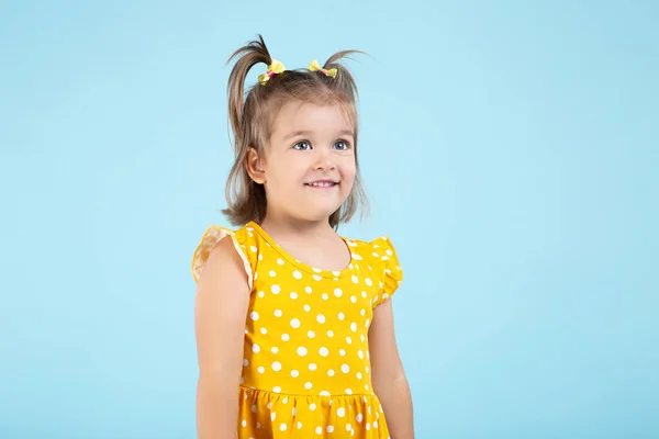 Söt liten flicka i gul klänning på blå bakgrund — Stockfoto