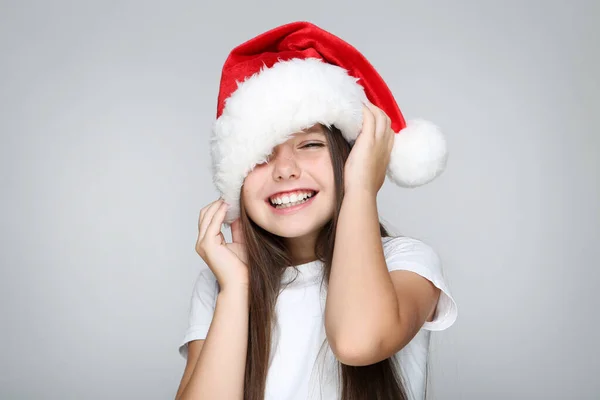 Маленькая девочка в рождественской шляпе на сером фоне — стоковое фото