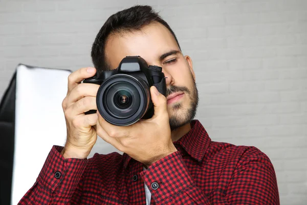 Joven fotógrafo con cámara y equipo de estudio en la espalda gris —  Fotos de Stock