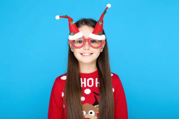Klein meisje in trui en kerstbril op blauwe achtergrond — Stockfoto