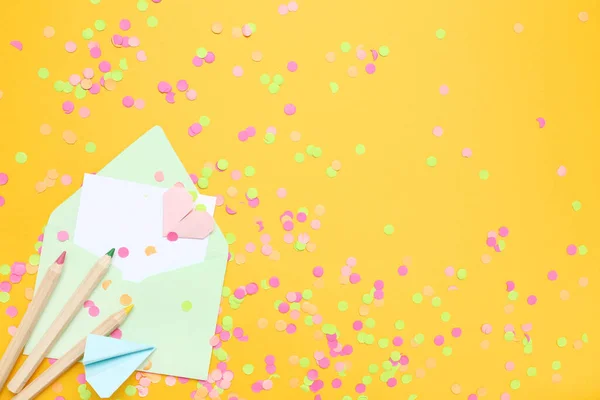 Kuvert med konfetti och pennor på gul bakgrund — Stockfoto