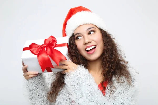 Noel Baba şapkalı güzel Amerikalı kadın gri arka planda hediye kutusu tutuyor. — Stok fotoğraf