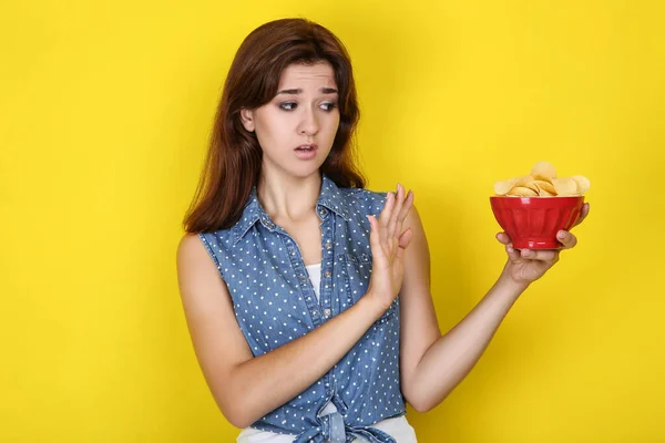 Ung kvinna med potatischips i skål på gul bakgrund — Stockfoto