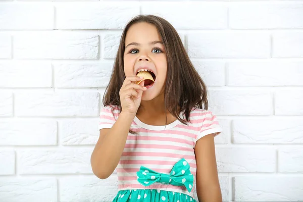Beautiful little girl eating potato chips on white brick wall ba — Zdjęcie stockowe