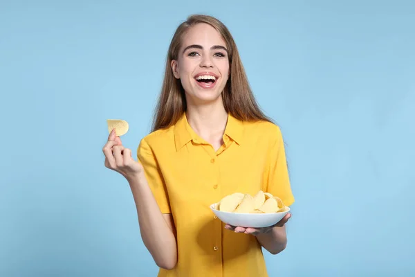 Молодая красивая девушка с картофельными чипсами в миске на синей спинке — стоковое фото