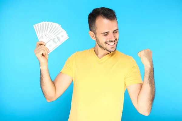 Joven hombre feliz sosteniendo billetes de dólar sobre fondo azul — Foto de Stock