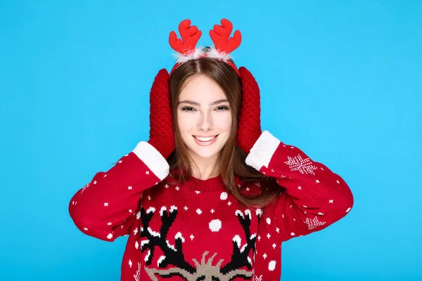 Mooie vrouw in kerst trui, handschoenen en rode horens op blauwe achtergrond — Stockfoto