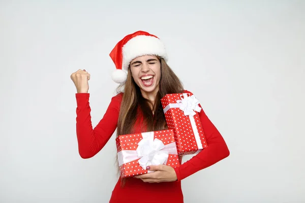 Güzel bir kadın Noel Baba şapkası takıyor ve gri üzerinde hediye kutuları taşıyor. — Stok fotoğraf