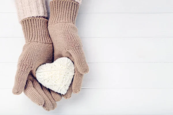 Manos en manoplas de punto que sostienen el corazón sobre una mesa de madera blanca —  Fotos de Stock