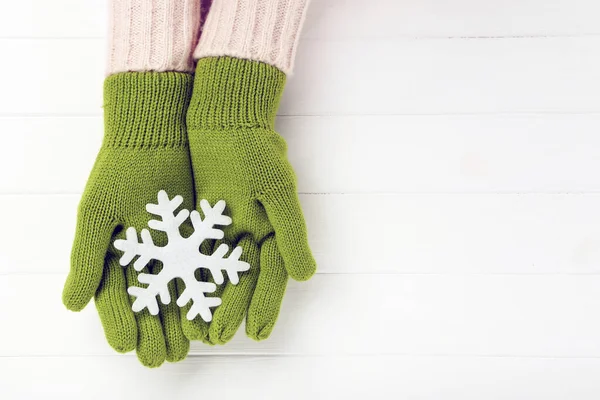 Hands in knitted mittens holding snowflake on white wooden table — Stock Photo, Image