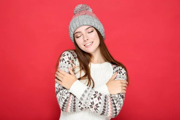 Beautiful woman in sweater and hat on red background