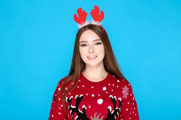 Mooie vrouw in kerst trui en rode horens op blauwe achtergrond — Stockfoto