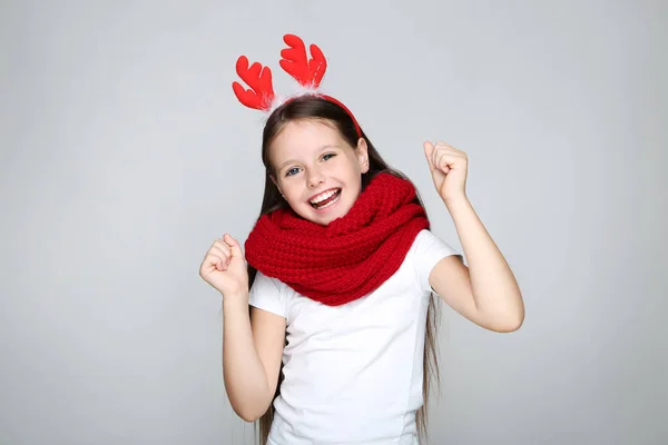 Klein meisje in kerstmis rode hoorns en gebreide sjaal op grijze achtergrond — Stockfoto