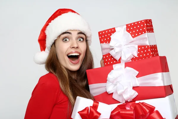 Mulher bonita usando chapéu de Papai Noel e segurando caixas de presente em cinza — Fotografia de Stock